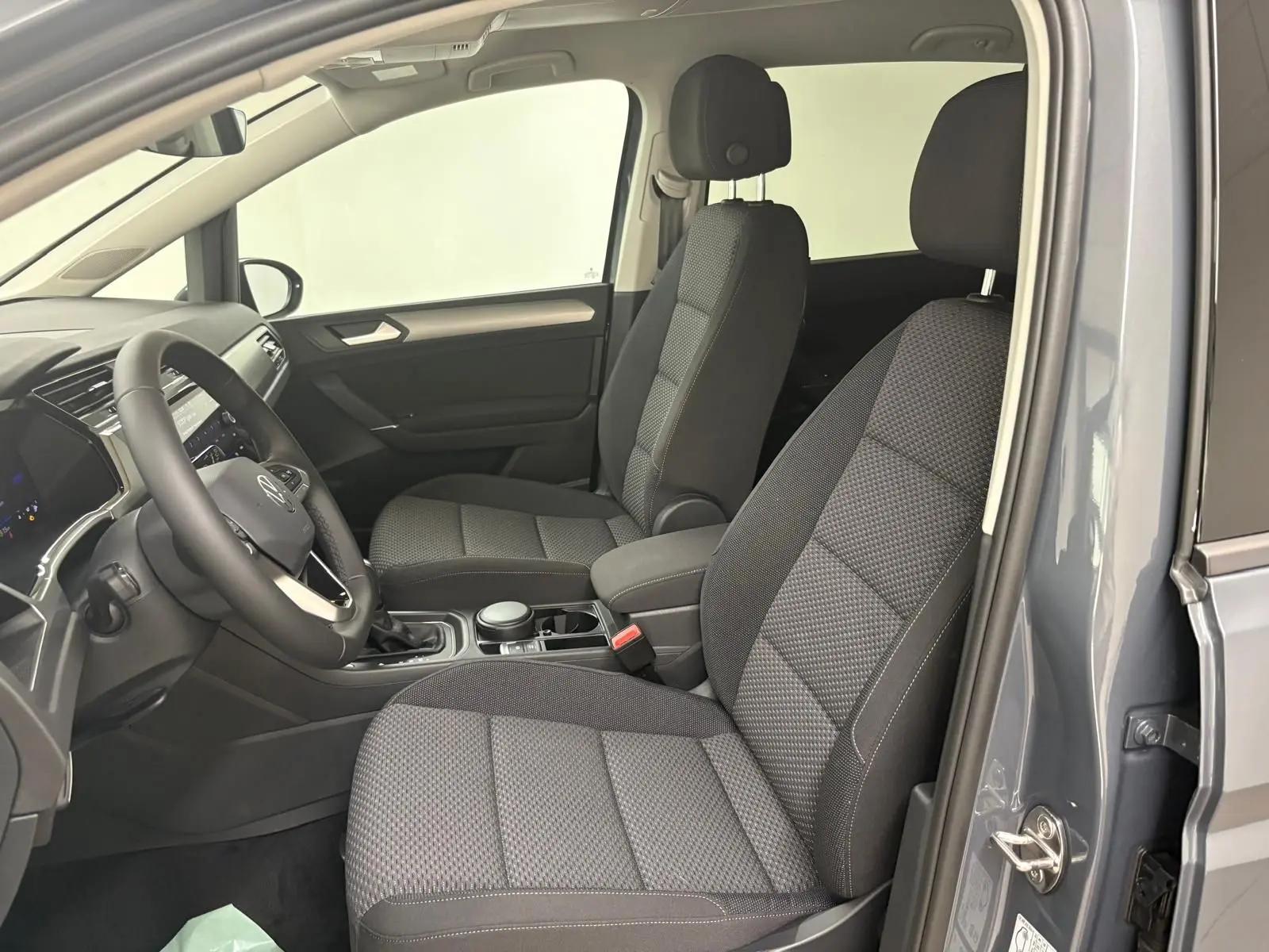 Vue intérieure côté conducteur du Volkswagen Touran gris dauphin 2025, montrant les sièges avant en tissu et le tableau de bord.