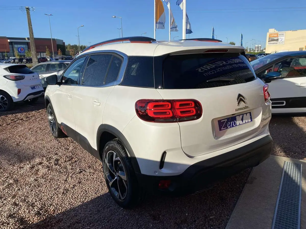 Vue 3/4 arrière droite d'un Citroën C5 Aircross blanc nacré avec barres de toit Deep Red anodisé et jantes bi-ton.