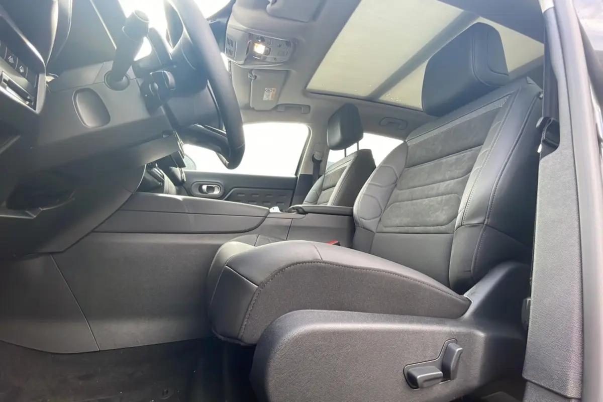Intérieur du Citroën C5 Aircross Hybrid 2025 vu côté conducteur, sièges noirs et toit panoramique lumineux.