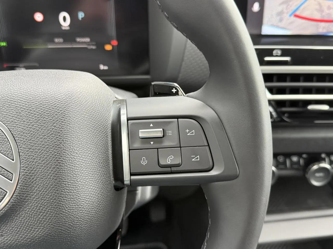 Gros plan sur les commandes au volant côté droit du Citroën C4 hybride 2025 avec tableau de bord numérique en arrière-plan.