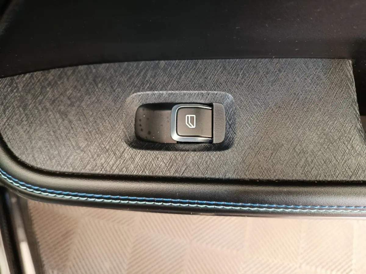 Bouton de commande de lève-vitre sur porte intérieure avec surpiqûres bleues, intérieur noir du Link & Co 01 hybride rechargeable.