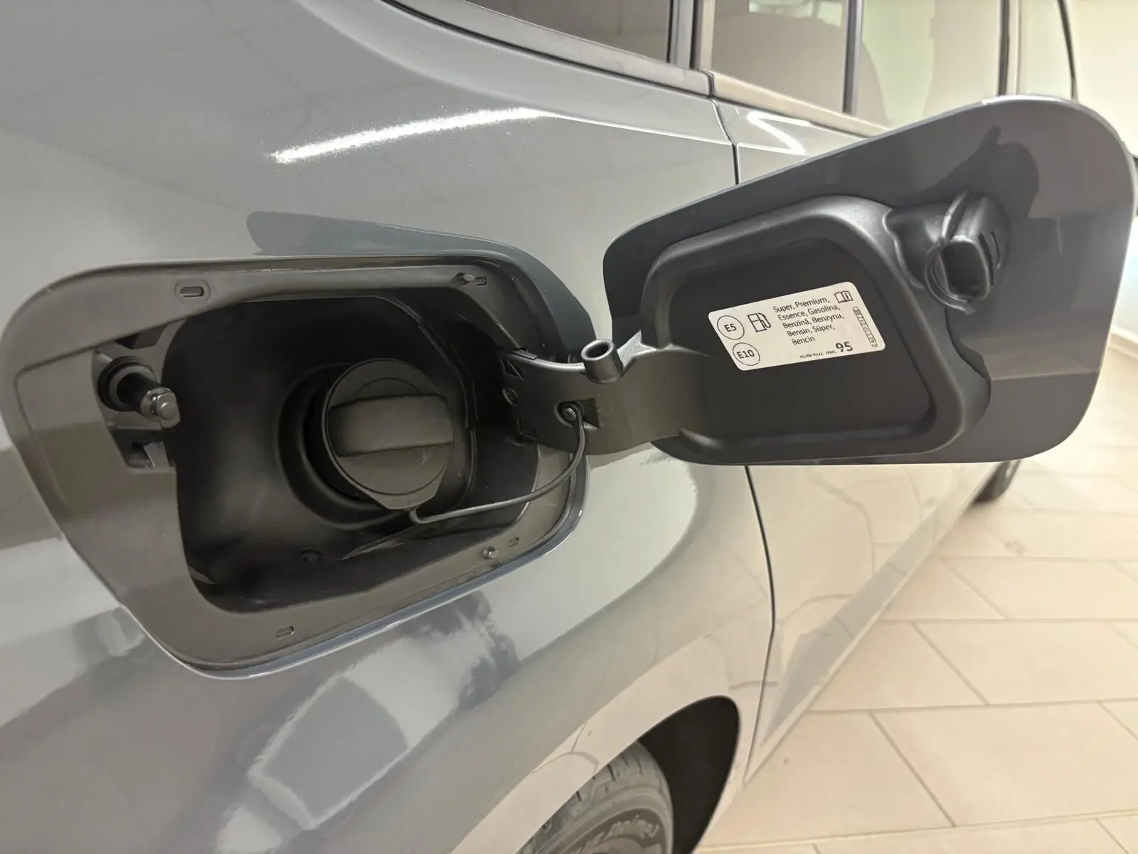 Gros plan sur la trappe à carburant ouverte côté gauche du Volkswagen Touran gris dauphin 2025 essence.