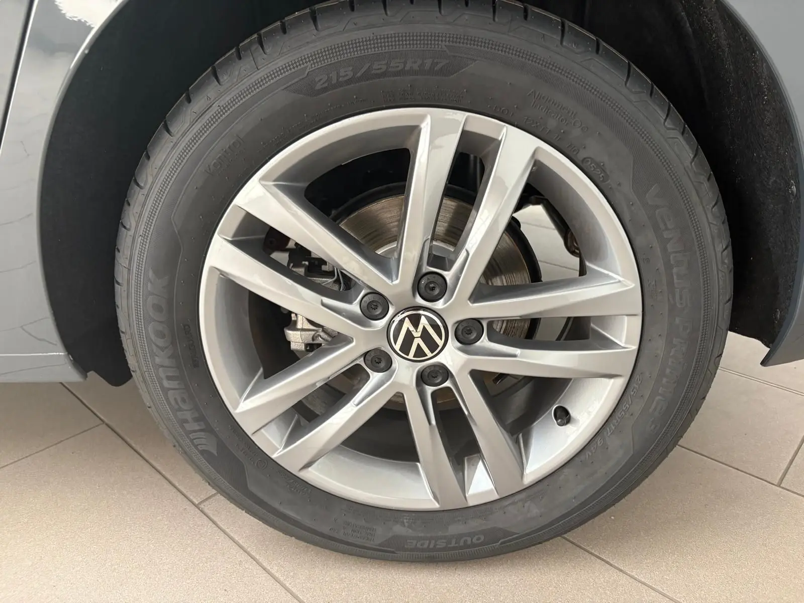 Gros plan sur la roue avant droite du Volkswagen Touran gris dauphin avec jante alliage 17 pouces et logo VW central.