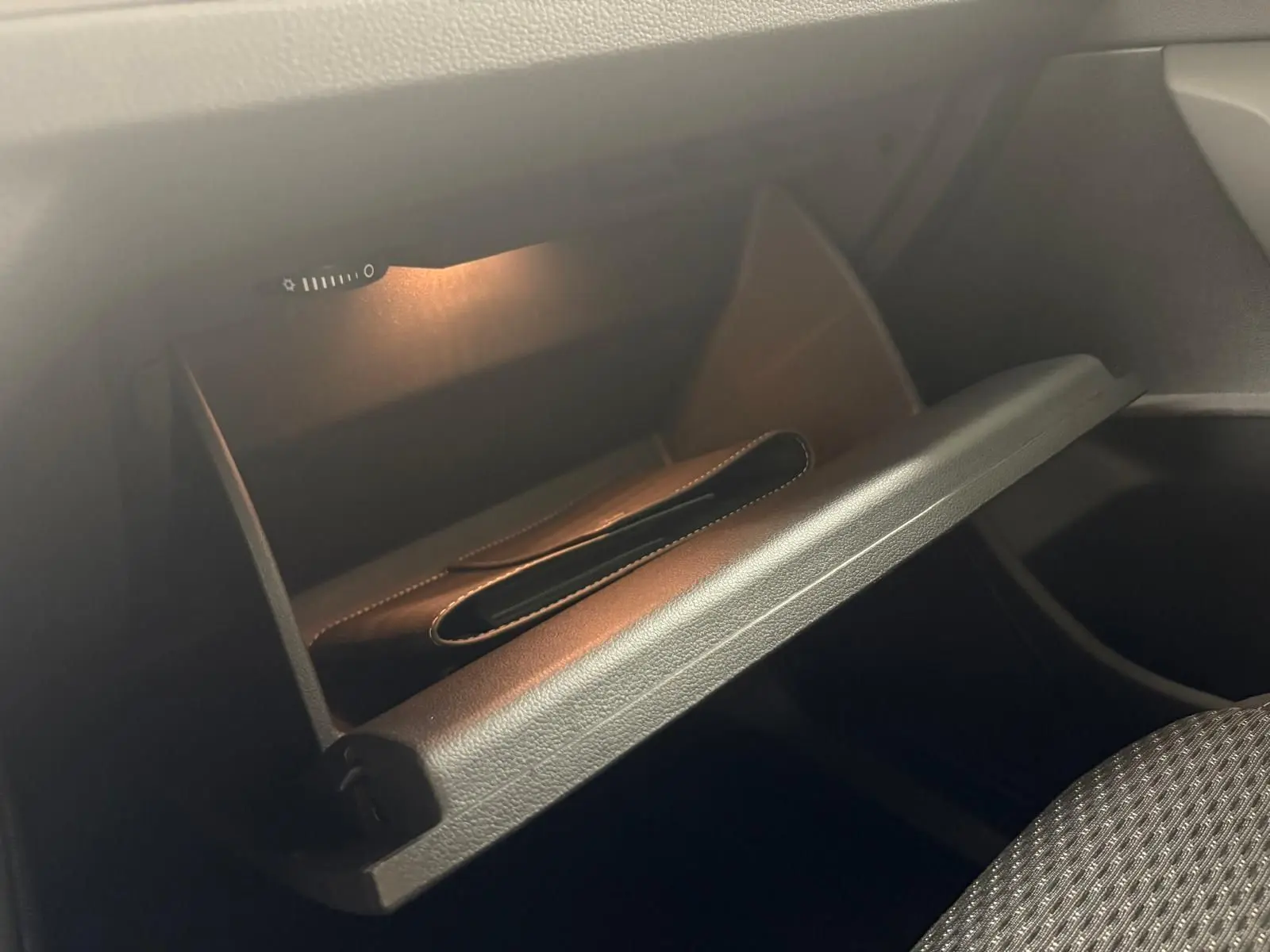 Gros plan sur la boîte à gants ouverte éclairée à l'intérieur du Volkswagen Touran gris Dauphin 2025.