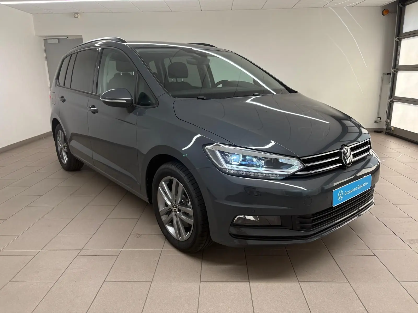Vue 3/4 avant droit d'un Volkswagen Touran gris dauphin 2025 avec feux LED et jantes alliage 17 pouces.