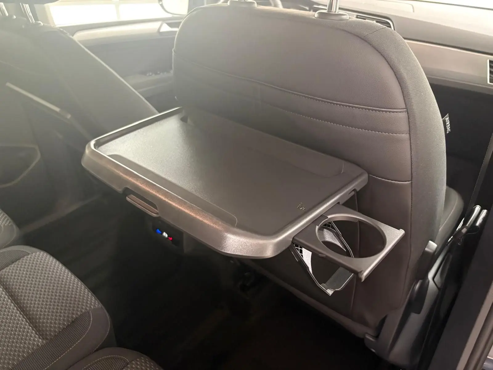 Tablette rabattable avec porte-gobelet fixée au dossier du siège avant dans l'habitacle du Volkswagen Touran gris dauphin.