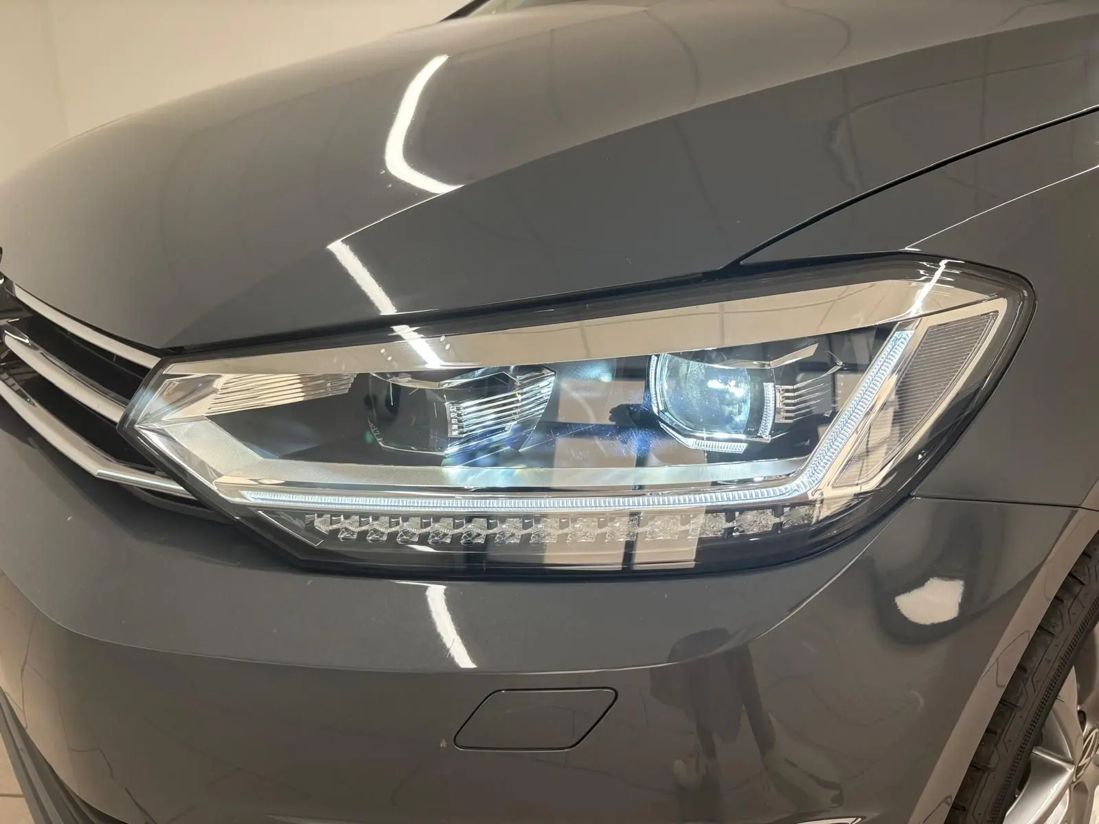 Gros plan sur le phare avant droit du Volkswagen Touran gris dauphin 2025 avec éclairage LED distinctif.