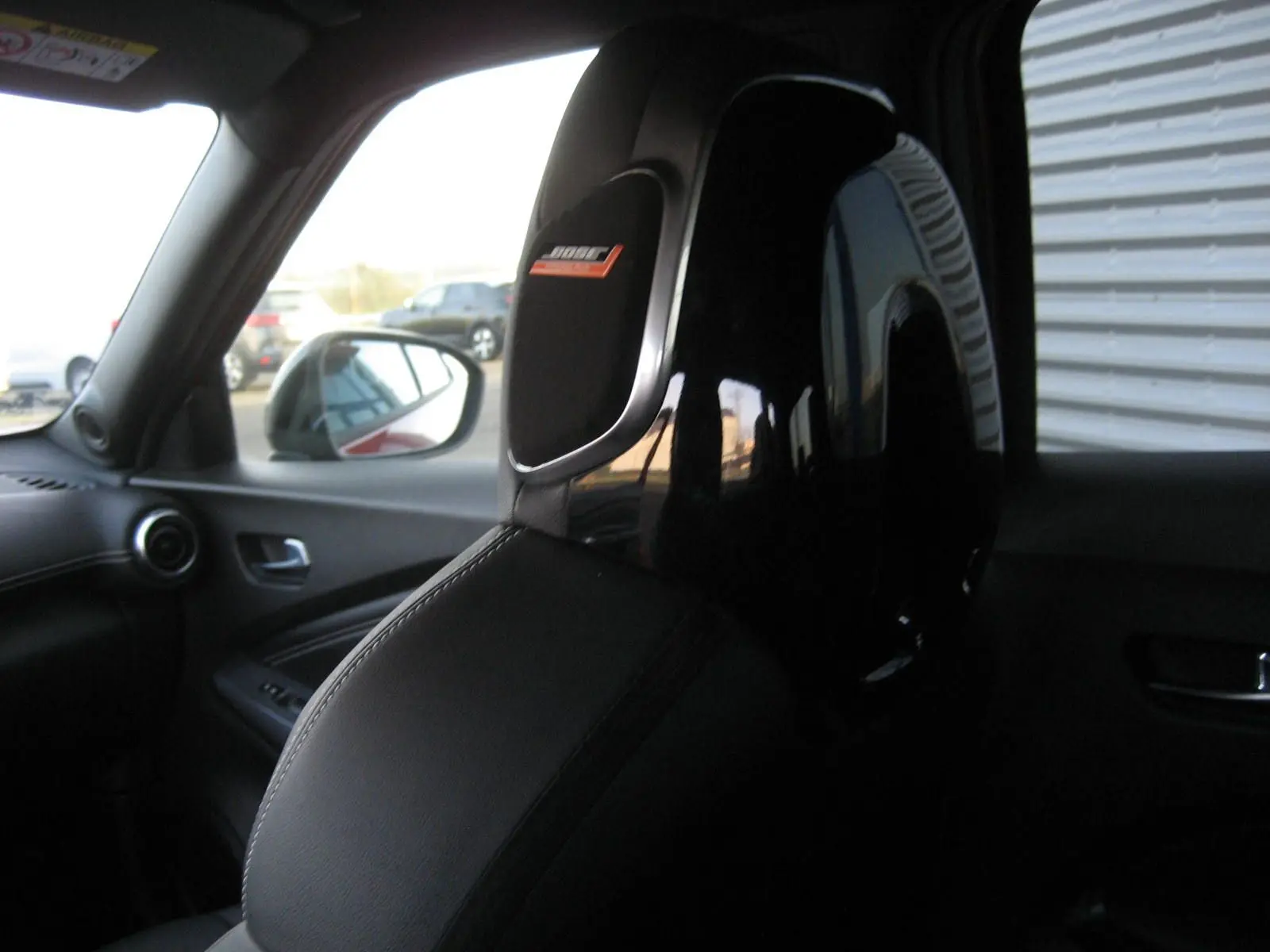 Gros plan sur l'appui-tête avant gauche noir brillant avec logo Bose, intérieur cuir du Nissan Juke 1.6 Hybrid 2024.