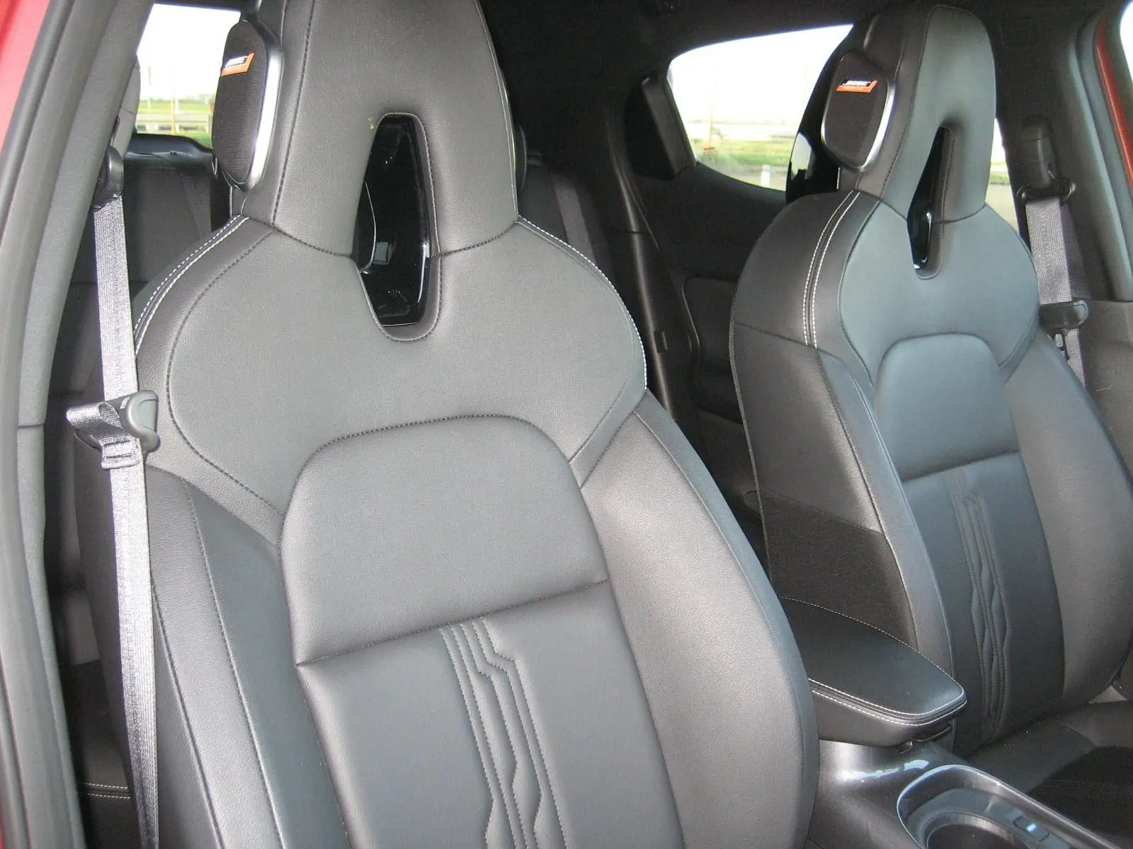 Vue intérieure rapprochée des sièges avant en cuir noir du Nissan Juke 1.6 Hybrid 143 Tekna rouge de 2024.