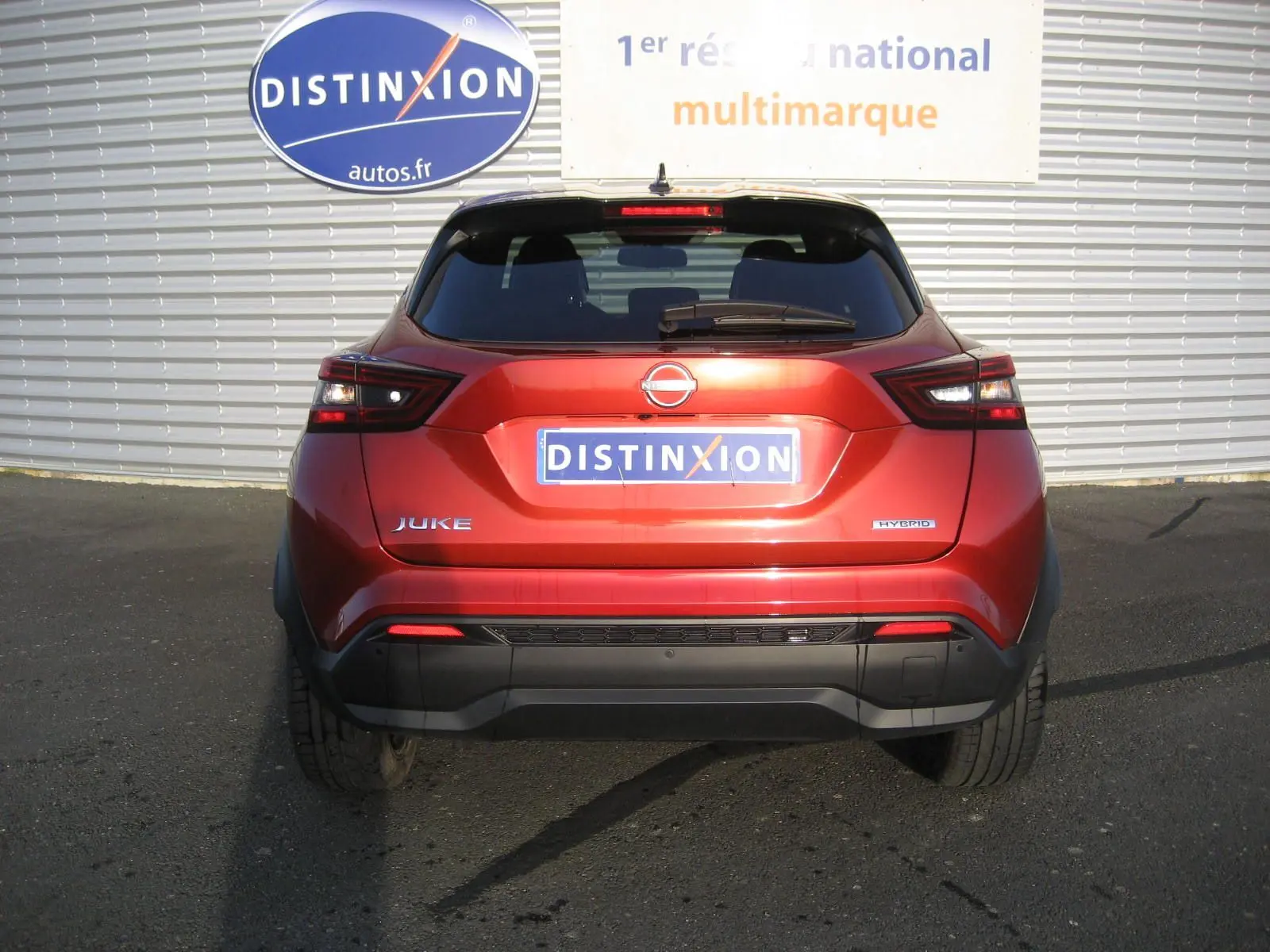 Vue arrière d'un Nissan Juke 1.6 Hybrid 143 Tekna rouge, avec feux arrière LED et logo hybride visible.