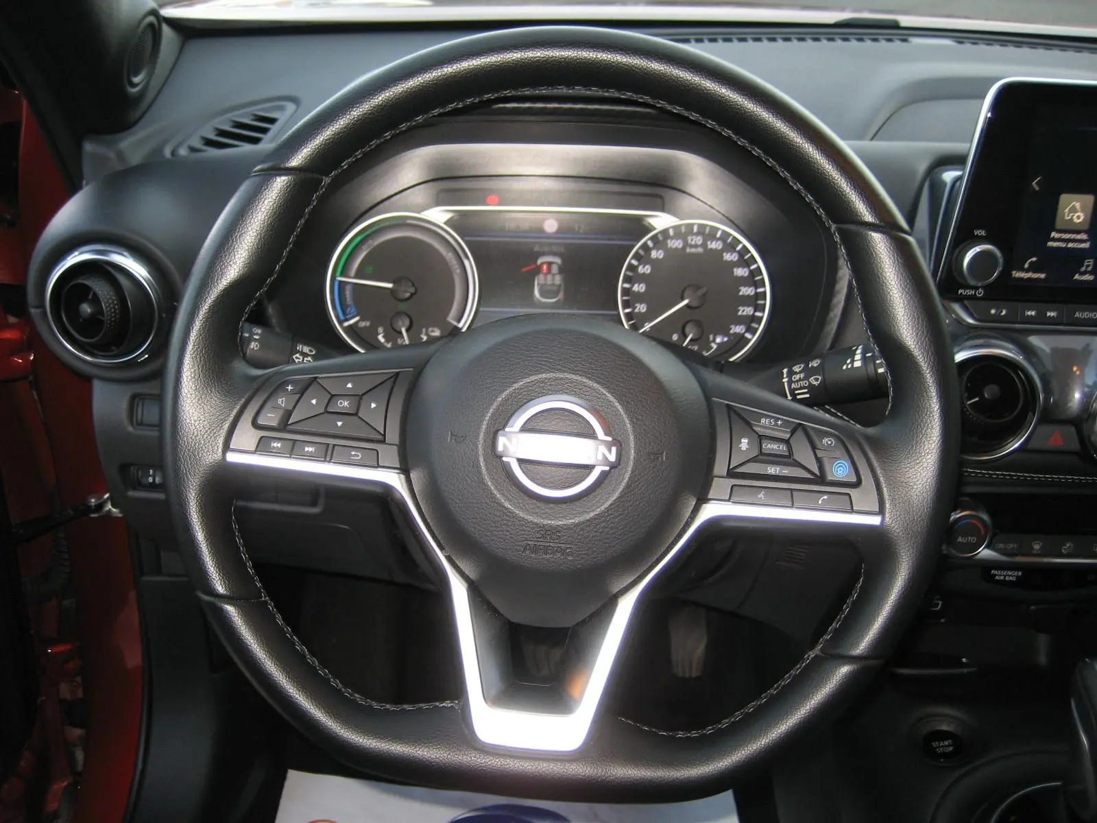 Vue rapprochée du volant en cuir noir du Nissan Juke rouge 2024, avec tableau de bord et écran tactile visibles.