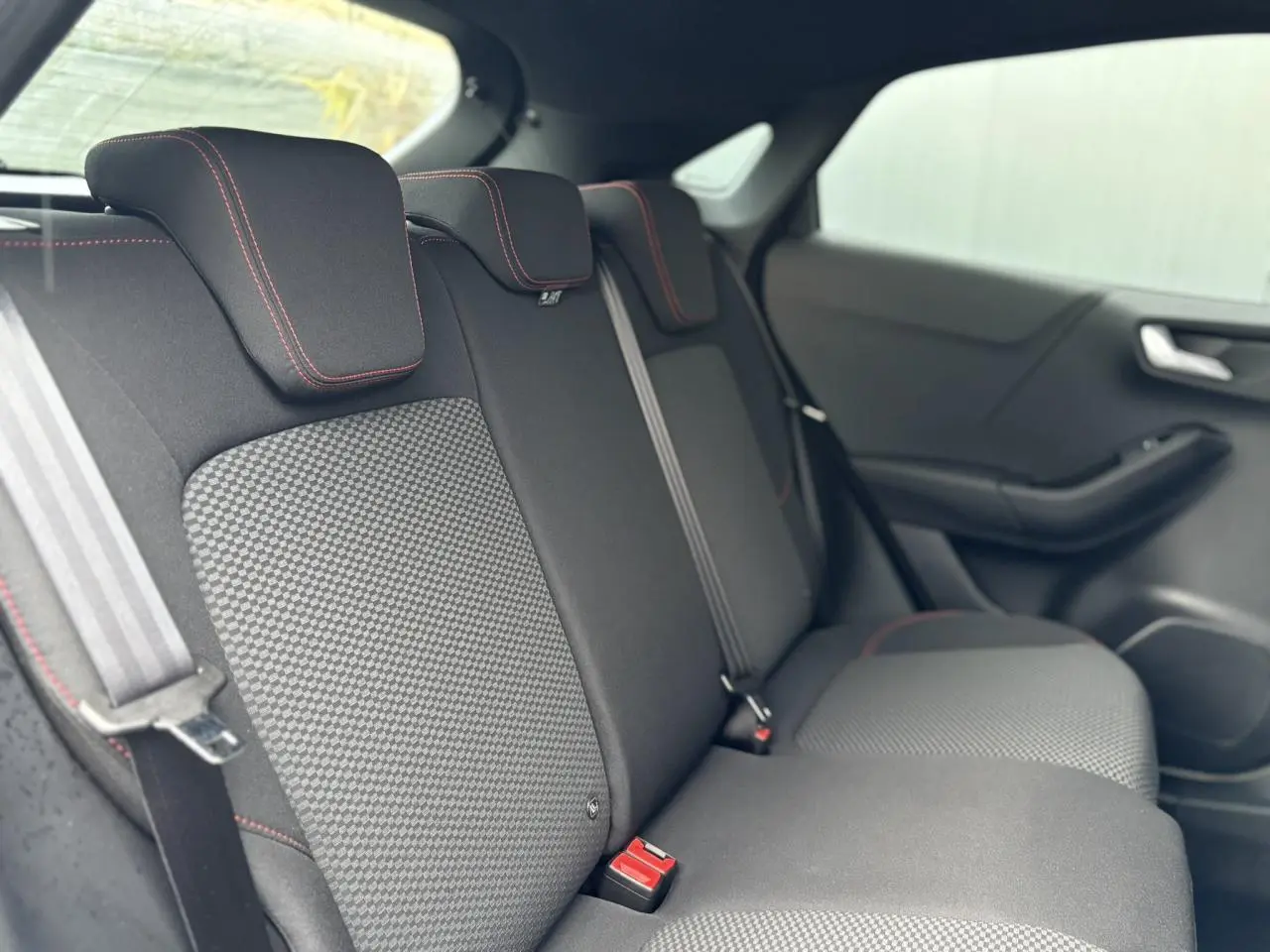 Vue intérieure du siège arrière droit de la Ford Puma 2023, tissu noir avec surpiqûres rouges et ceintures grises.