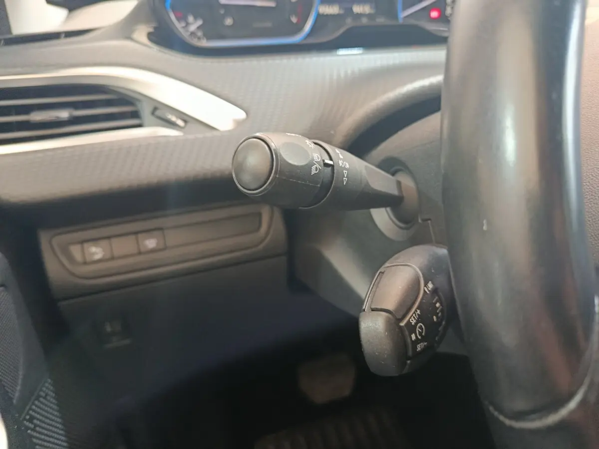 Gros plan sur la colonne de direction du Peugeot 2008 gris foncé, avec commandes de phares et régulateur de vitesse visibles.