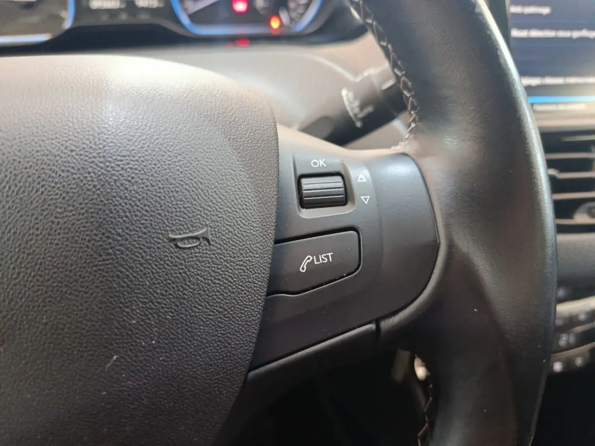 Gros plan sur le volant cuir noir côté droit du Peugeot 2008 gris foncé, avec commandes intégrées et tableau de bord en arrière-plan.