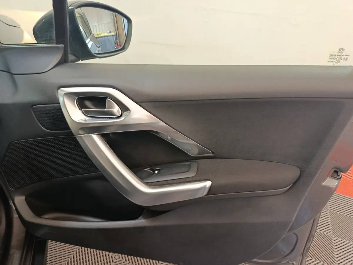 Vue intérieure côté gauche de la porte avant d'une Peugeot 2008 gris foncé avec poignée argentée et commande de vitre.