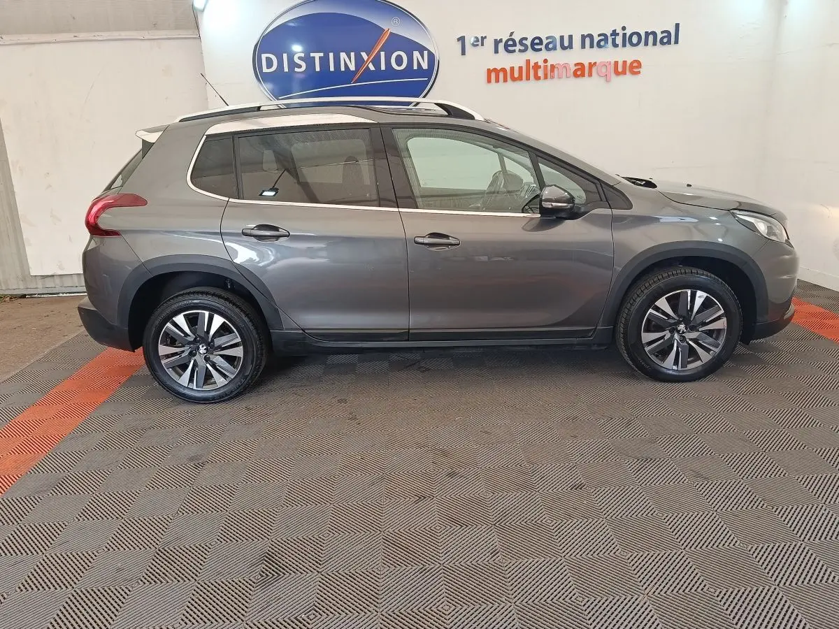 Peugeot 2008 gris foncé vue de profil côté gauche, avec jantes alliage et barres de toit chromées.