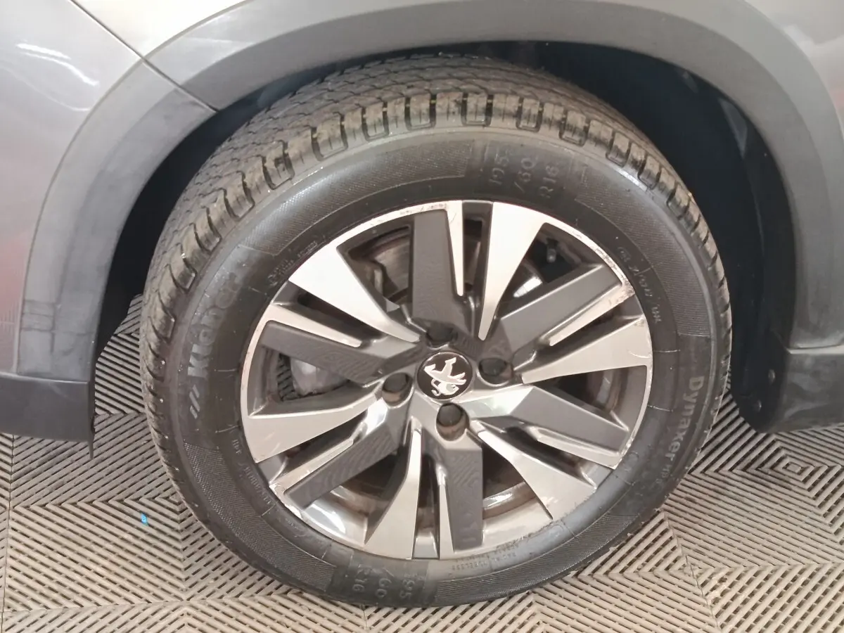 Gros plan sur la roue avant gauche d’un Peugeot 2008 gris foncé, mettant en valeur la jante alliage distinctive.