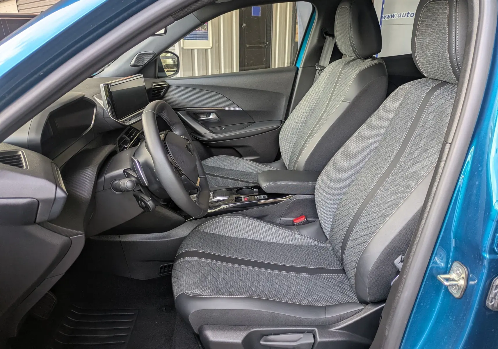 Vue intérieure côté conducteur de la Peugeot 2008 Hybrid 145 Allure bleu obsession, avec sellerie tissu gris et volant multifonction.