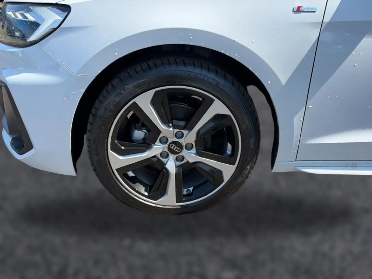 Gros plan sur la roue avant gauche et l’aile blanche de l’Audi A1 Sportback 30 TFSI S line avec jante alu bicolore.