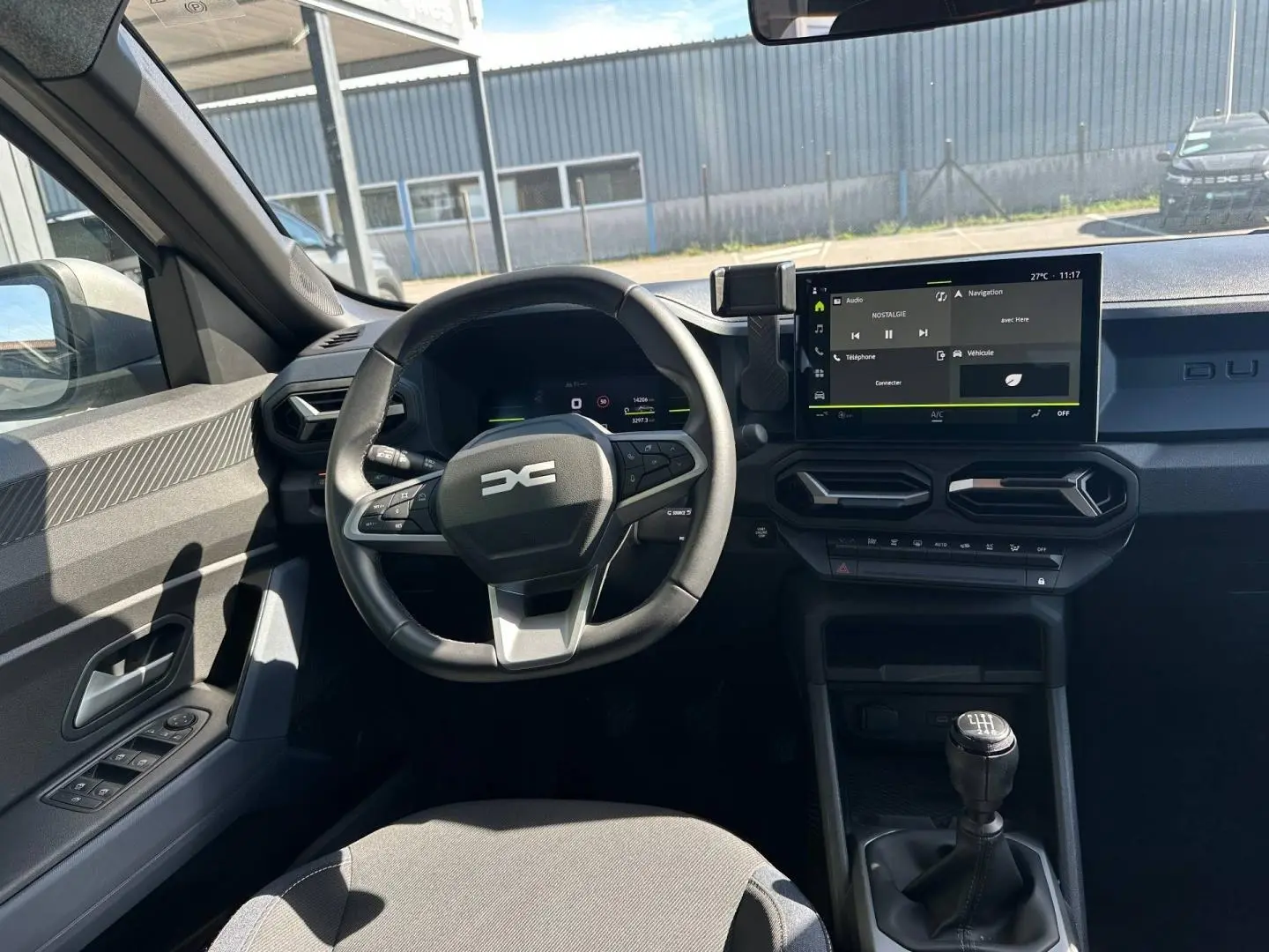 Vue intérieure côté conducteur du Dacia Duster 2025, montrant le volant multifonction, écran tactile et levier de vitesses manuel.