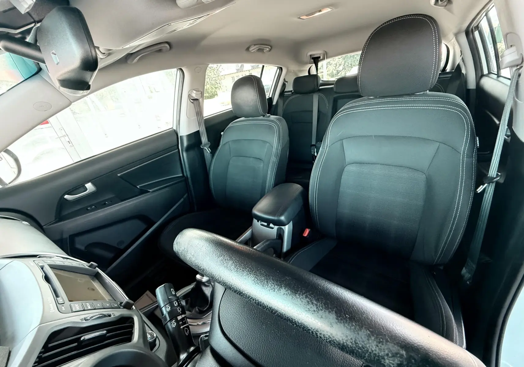 Vue intérieure du Kia Sportage 2015 montrant les sièges avant noirs en tissu et le tableau de bord côté gauche.