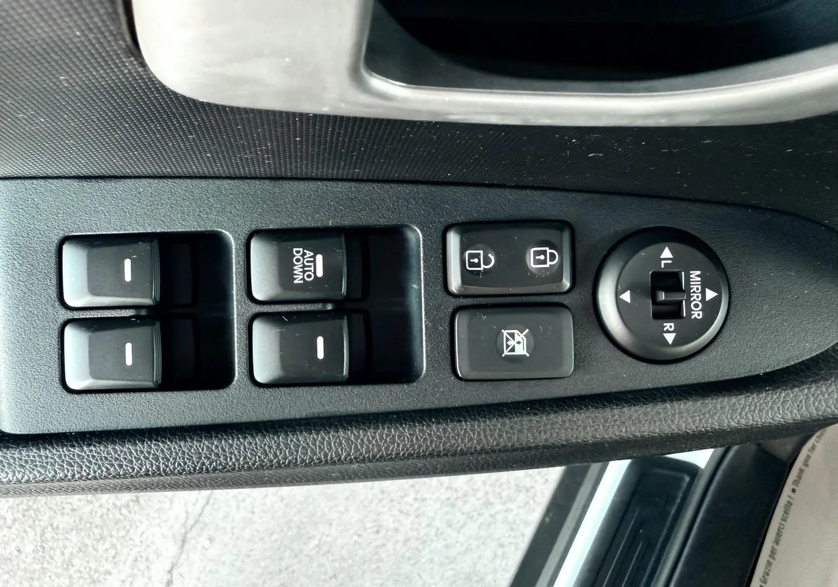 Panneau de commandes des vitres et rétroviseurs côté conducteur dans une KIA Sportage blanche de 2015.