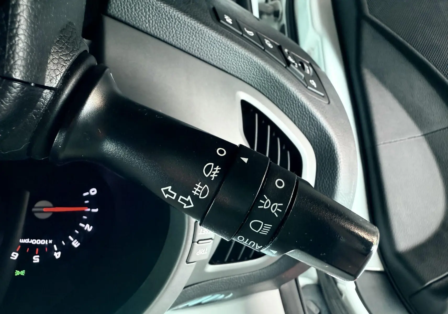 Gros plan sur la manette de commande des phares et clignotants dans l'habitacle d'un Kia Sportage blanc de 2015.