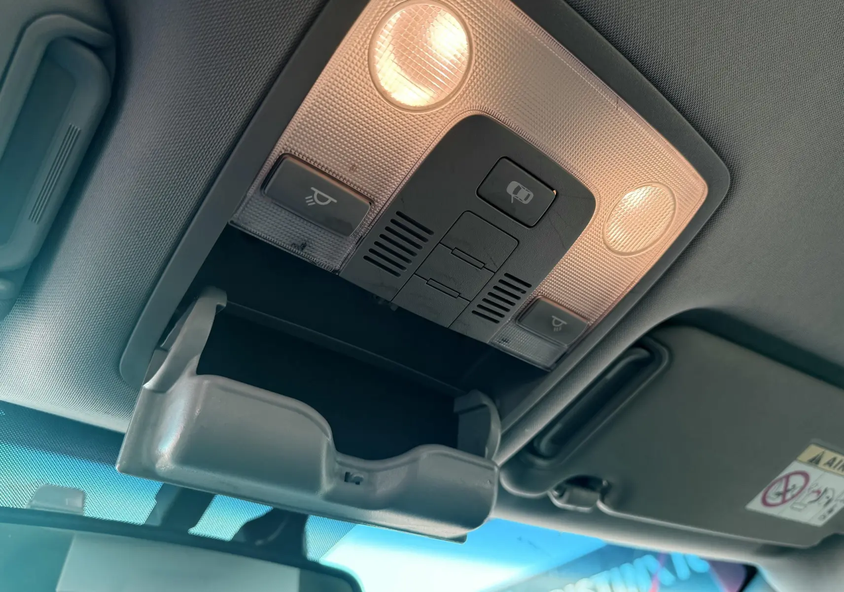 Plafonnier intérieur allumé avec rangement lunettes ouvert sur KIA SPORTAGE blanc, vue vers le pare-brise et rétroviseur.