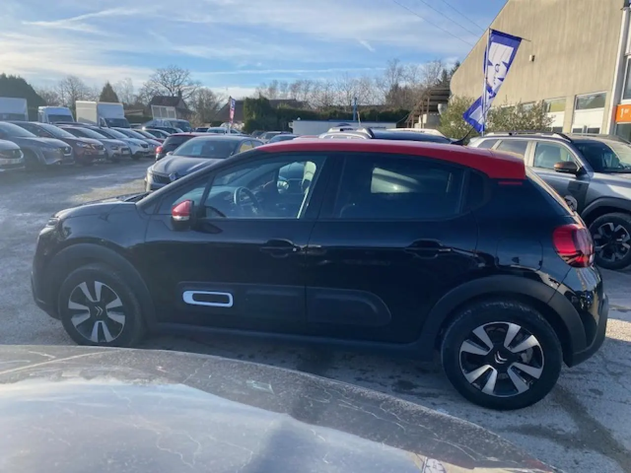 Profil côté gauche d'une Citroën C3 2023 noire avec toit rouge, stationnée en extérieur sous un ciel clair.
