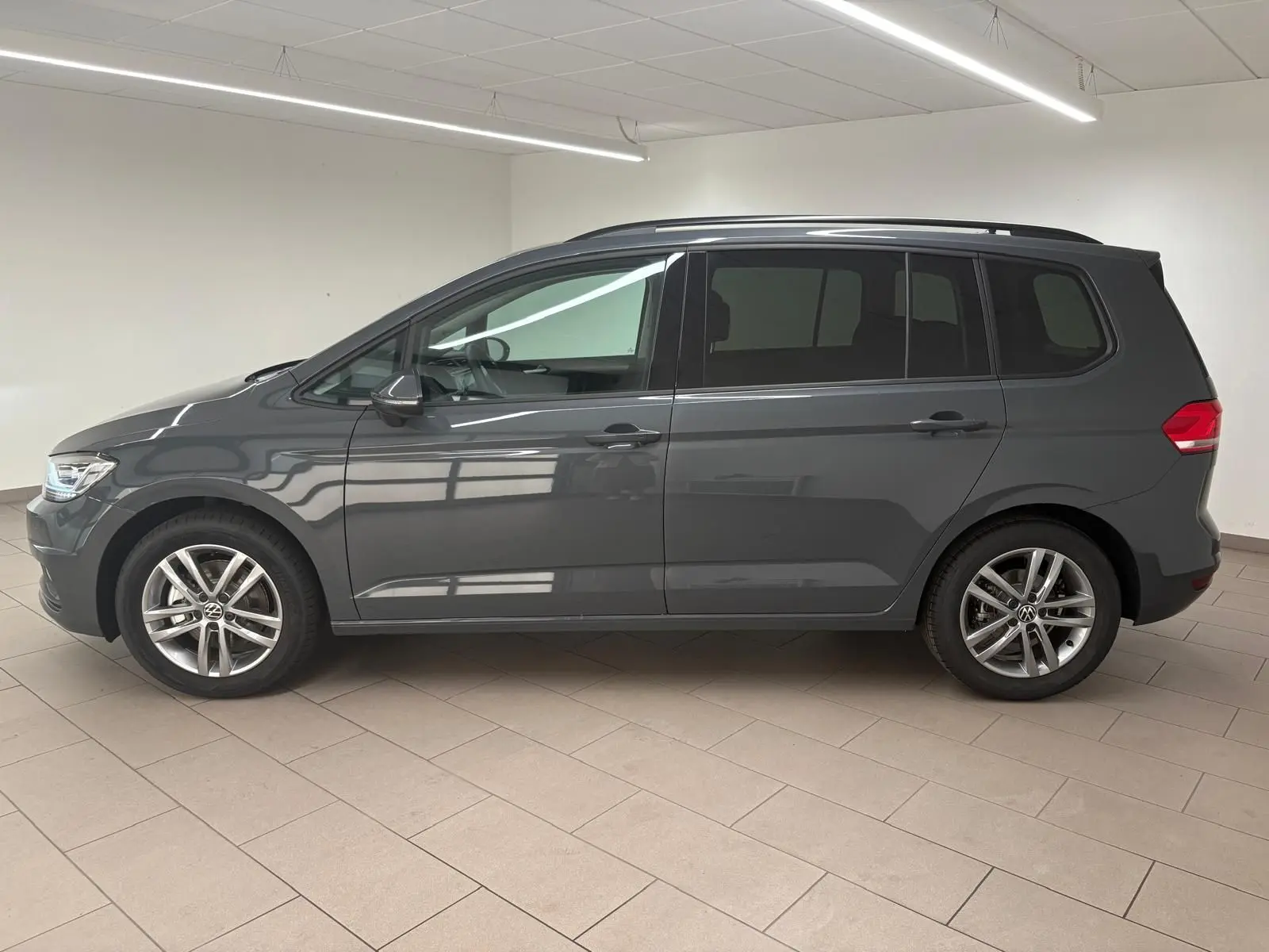 Profil côté gauche d'un Volkswagen Touran gris dauphin 2025, version 7 places avec jantes alliage 17 pouces en intérieur lumineux.