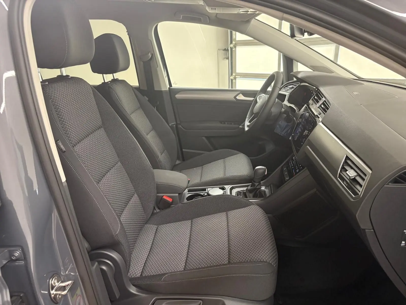 Intérieur du Volkswagen Touran 2025 gris dauphin, vue côté gauche montrant sièges avant et tableau de bord moderne.