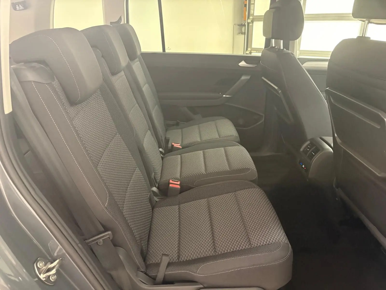 Vue latérale des sièges arrière en tissu gris foncé du Volkswagen Touran 2025 gris dauphin, avec appuie-têtes et ceintures visibles.