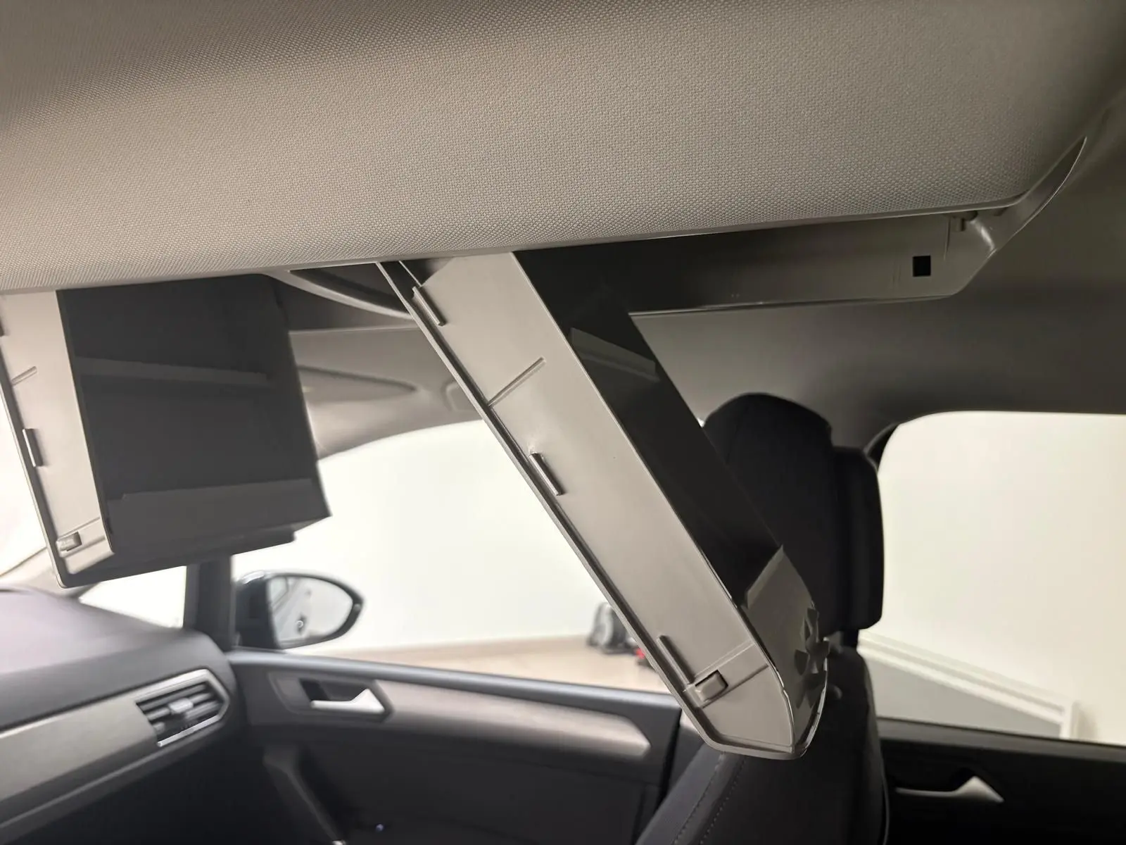 Intérieur du Volkswagen Touran 2025 montrant les écrans rabattables au plafond côté passager, ambiance sobre et moderne.