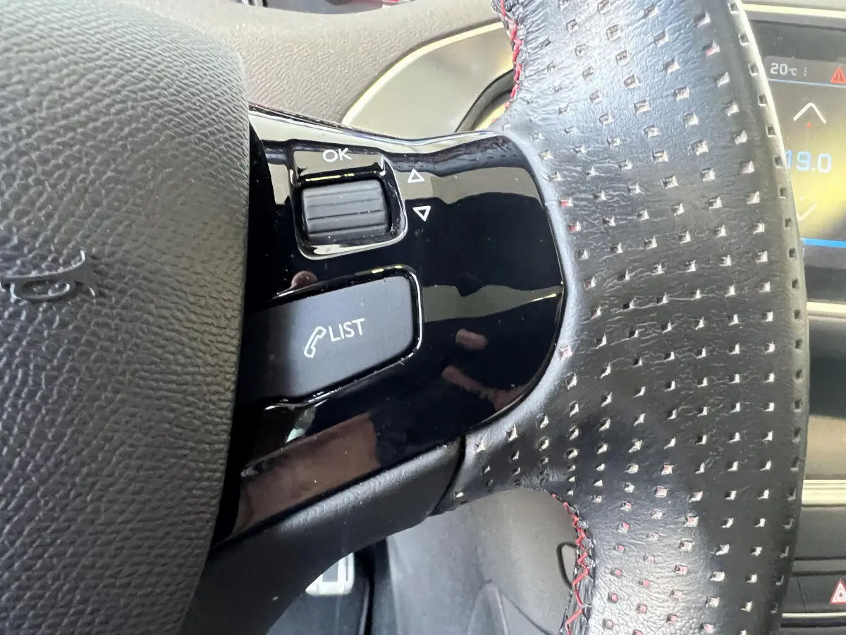 Gros plan sur le volant cuir perforé avec commandes intégrées du Peugeot 308 GT Line rouge de 2019.
