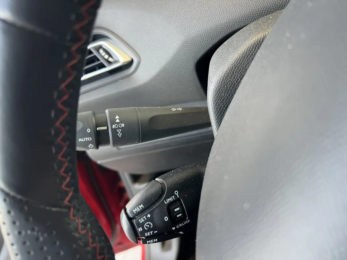 Gros plan sur commandes au volant cuir noir avec surpiqûres rouges dans Peugeot 308 GT Line rouge, côté gauche.