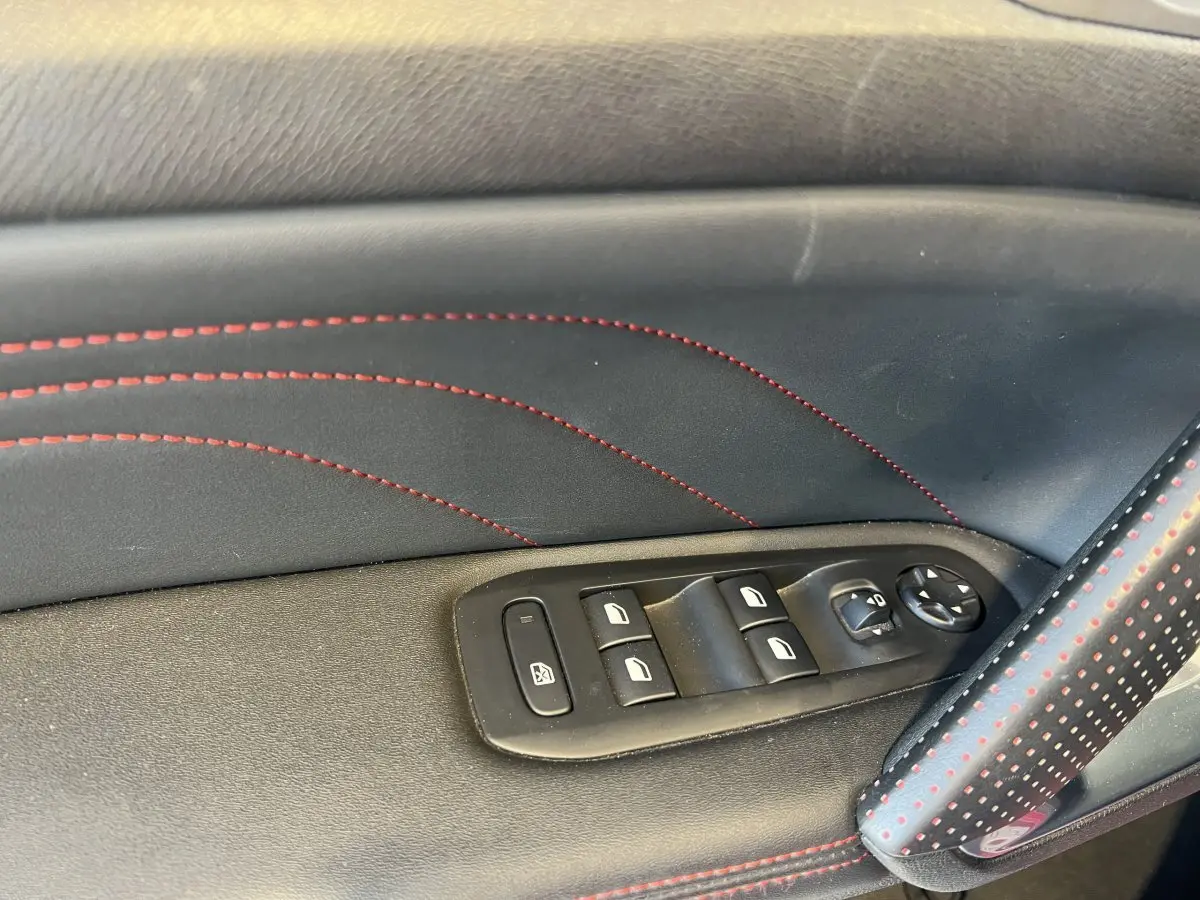 Gros plan sur la commande des vitres électriques côté conducteur avec surpiqûres rouges dans une Peugeot 308 GT Line rouge.