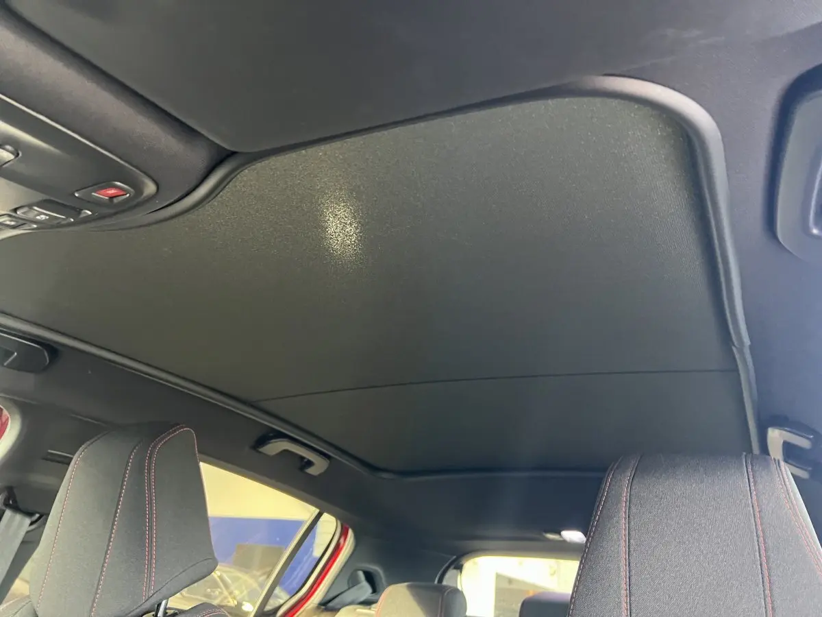 Vue intérieure du toit noir et des appuie-têtes avant avec surpiqûres rouges d'une Peugeot 308 GT Line rouge.
