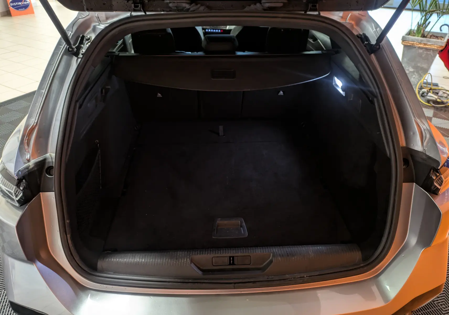 Vue arrière du coffre ouvert d'une Peugeot 308 SW Hybrid 145 gris, montrant l'espace de chargement vide et l'éclairage intérieur.