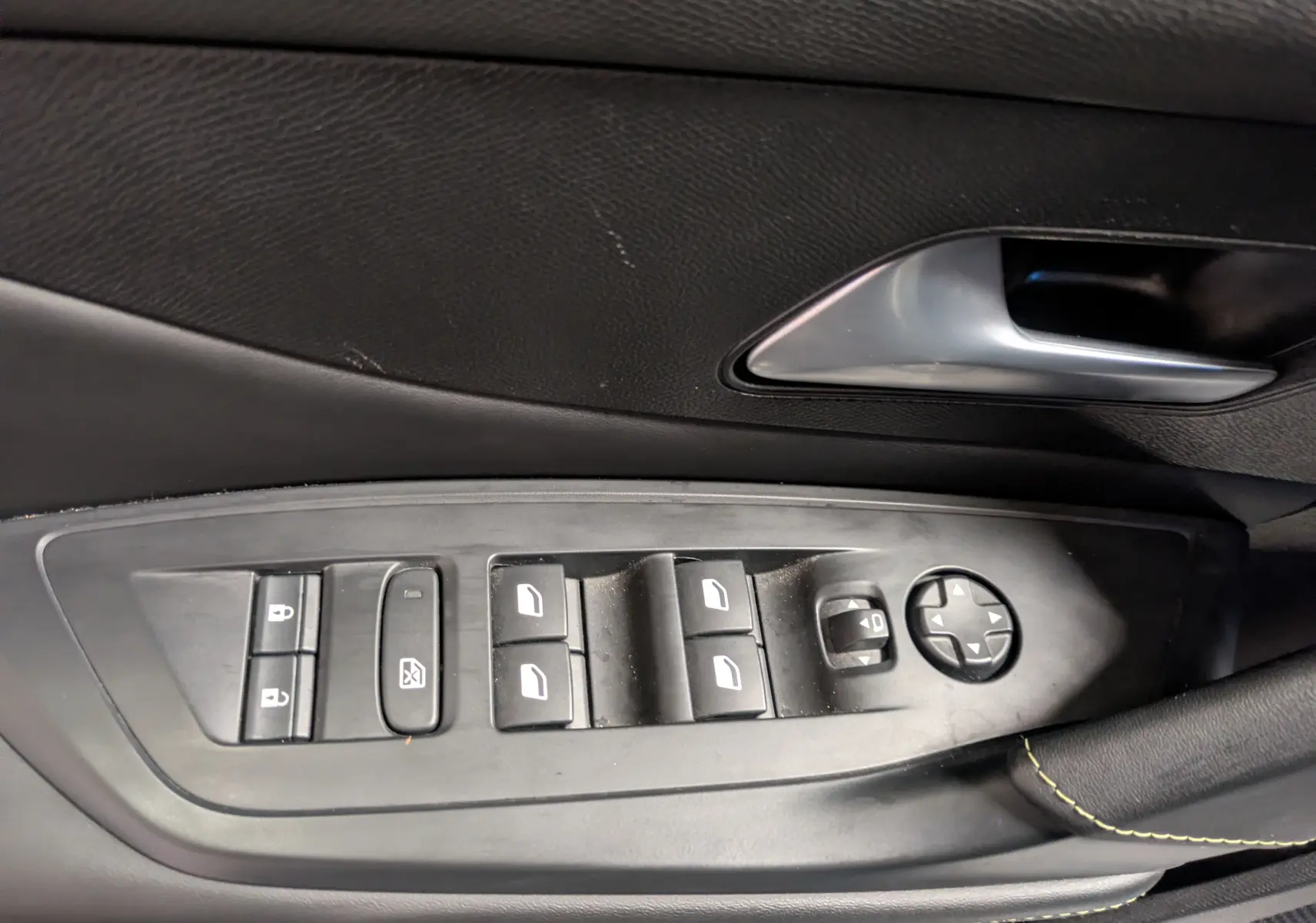 Gros plan sur la commande des vitres et rétroviseurs côté conducteur d’un Peugeot 308 SW gris, intérieur noir.