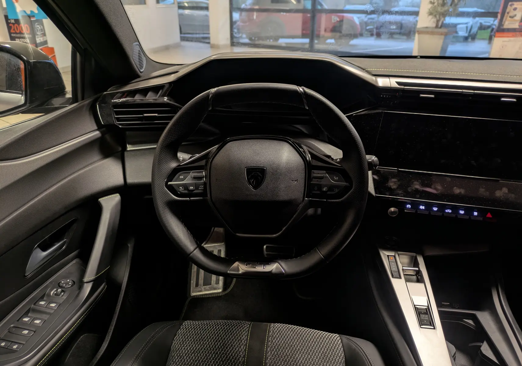 Vue intérieure centrée sur le volant GT et la console moderne du Peugeot 308 SW Hybrid gris, avec écran tactile et commandes intégrées.
