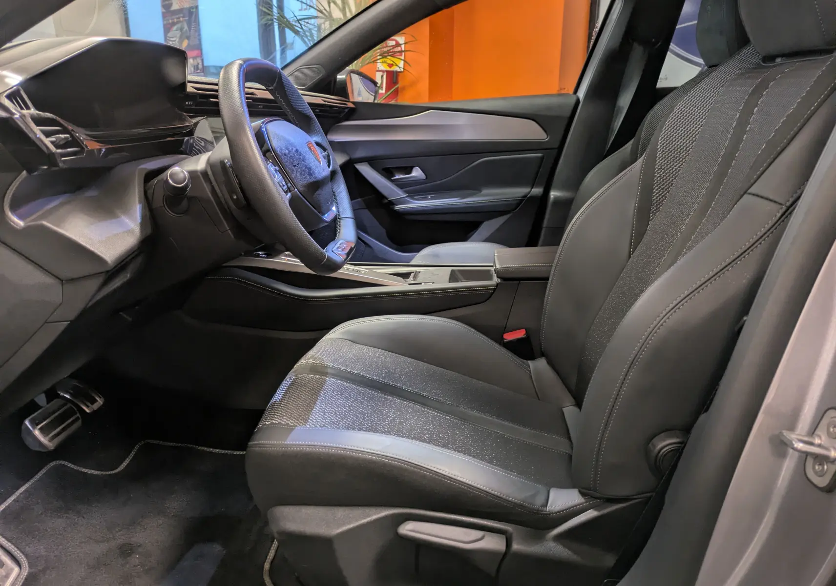 Intérieur côté conducteur de la Peugeot 308 SW Hybrid gris 2025, avec sellerie tri-matières et volant compact.