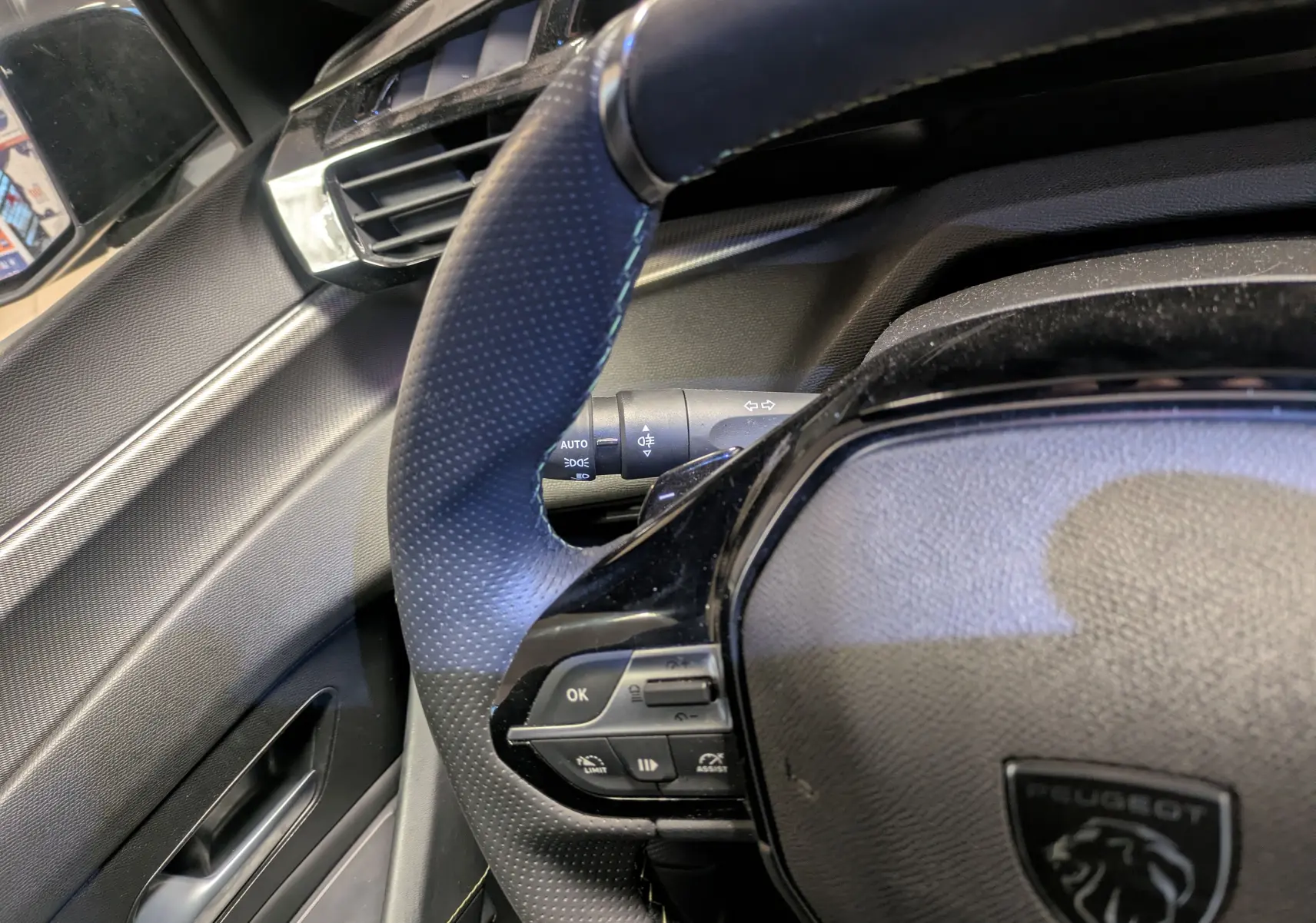 Gros plan sur le volant cuir perforé et les commandes multifonctions du Peugeot 308 SW Hybrid gris, côté conducteur.