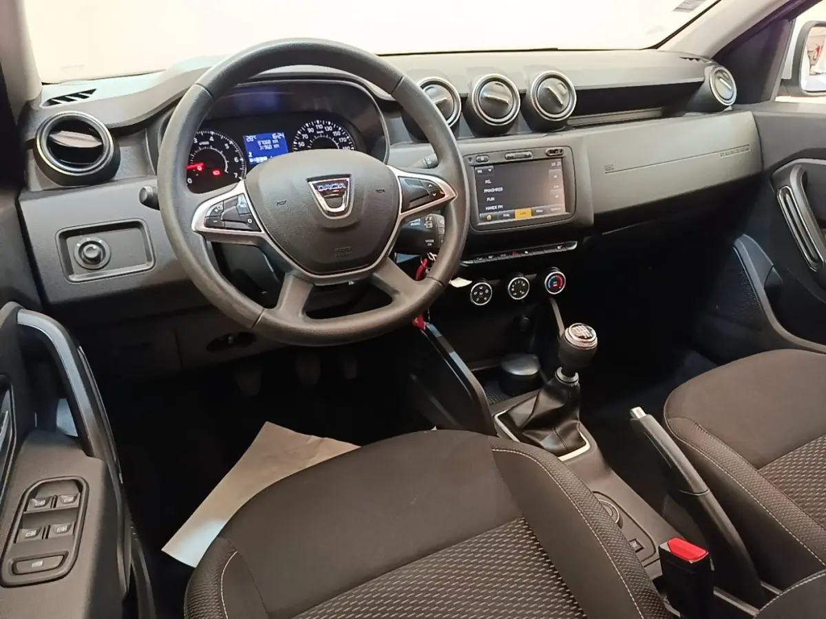 Vue intérieure côté conducteur du tableau de bord et volant cuir synthétique du Dacia Duster blanc de 2021.