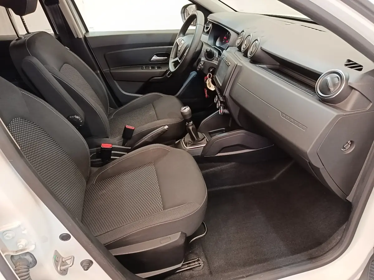 Vue intérieure côté conducteur du Dacia Duster blanc 2021, montrant sièges noirs, volant multifonctions et tableau de bord épuré.