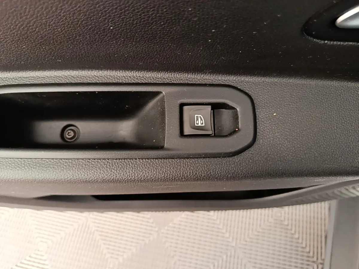 Gros plan sur le bouton de commande de vitre électrique côté conducteur du Dacia Duster blanc, intérieur noir.