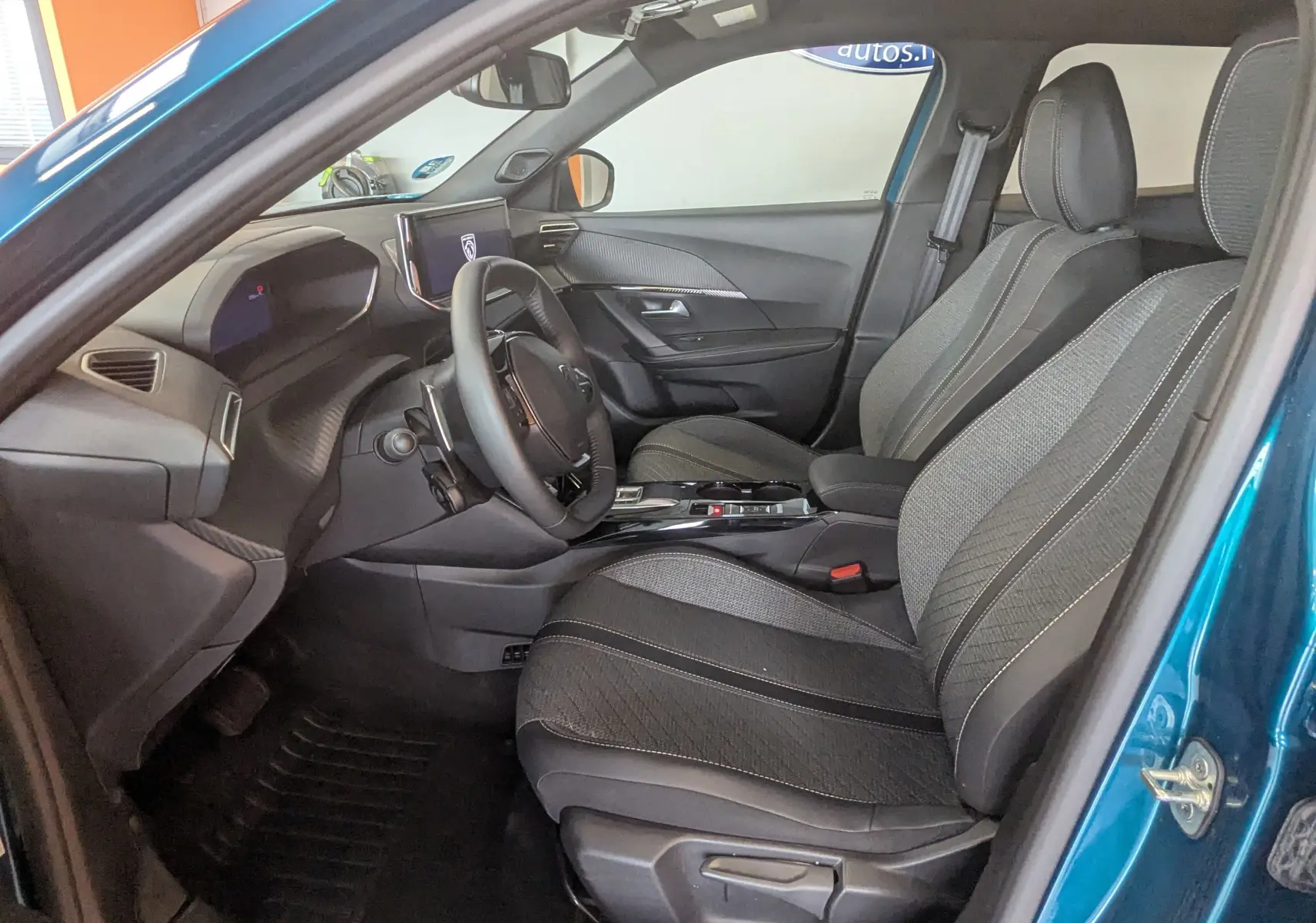 Vue intérieure côté conducteur du Peugeot 2008 Hybrid 145 bleu obsession, avec sièges tissu gris et tableau de bord moderne.