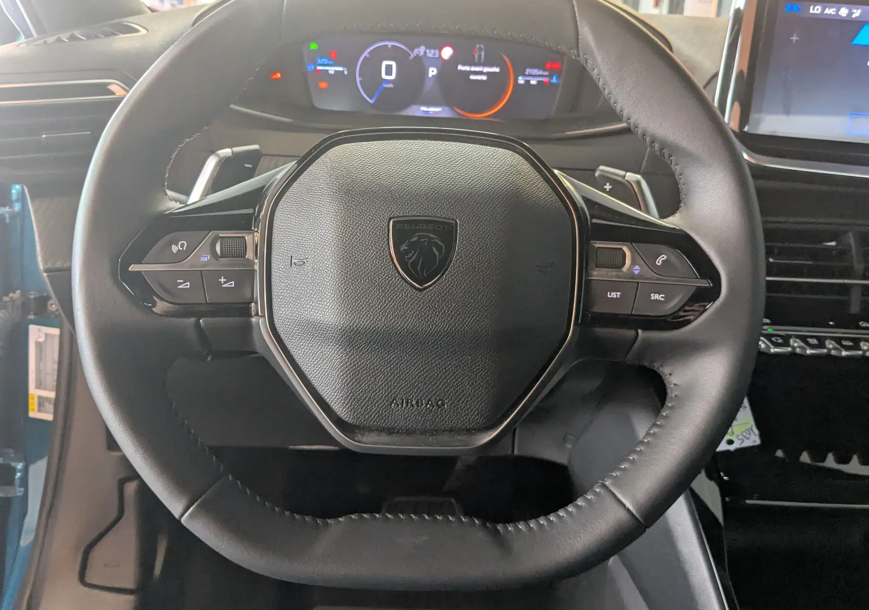 Vue rapprochée du volant cuir noir du Peugeot 2008 Hybrid 145 avec commandes intégrées et tableau de bord numérique.