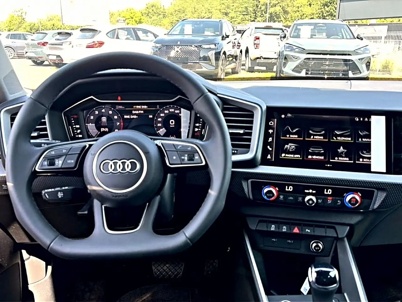 Vue intérieure centrée sur le volant multifonction et l'écran tactile du tableau de bord de l'Audi A1 Sportback blanc/noir.