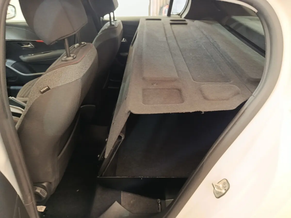 Vue intérieure côté droit du coffre ouvert de la Peugeot 208 blanche, montrant le rangement sous la tablette arrière.