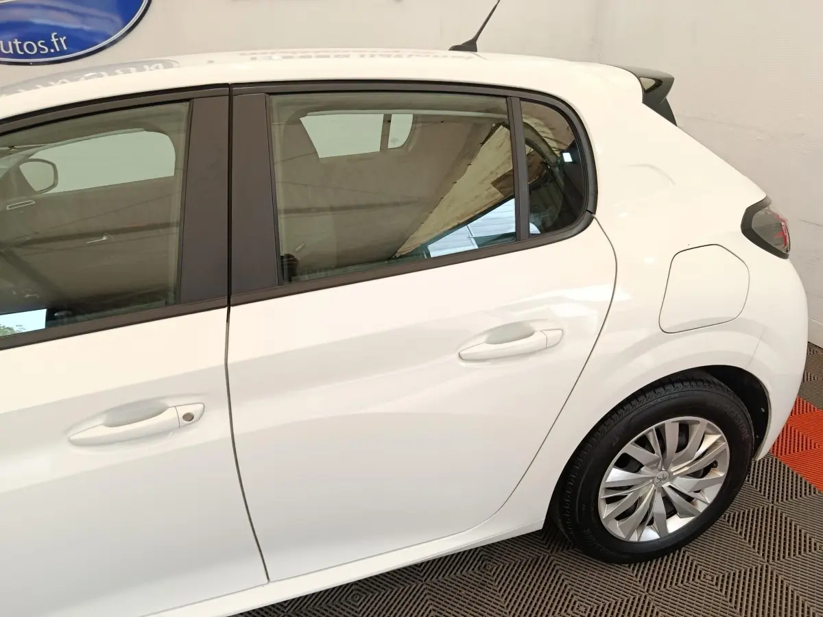 Vue latérale droite sur la partie arrière d’une Peugeot 208 blanche, avec jante alliage et porte essence visible.